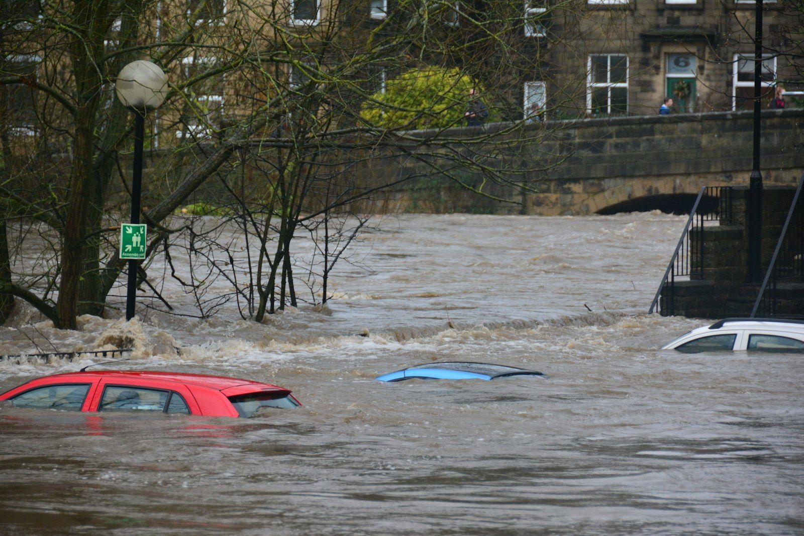 Aerial view of a suburban street partially submerged in floodwater, rooftops barely visible above brown water.